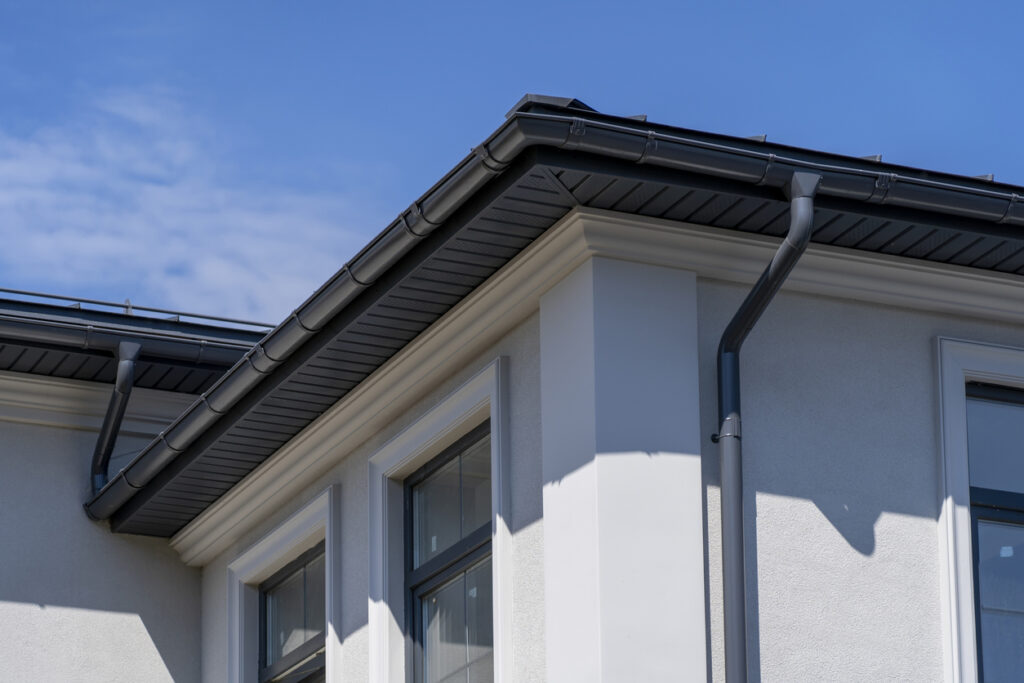Corner of house with windows, new gray metal tile roof and rain gutter.