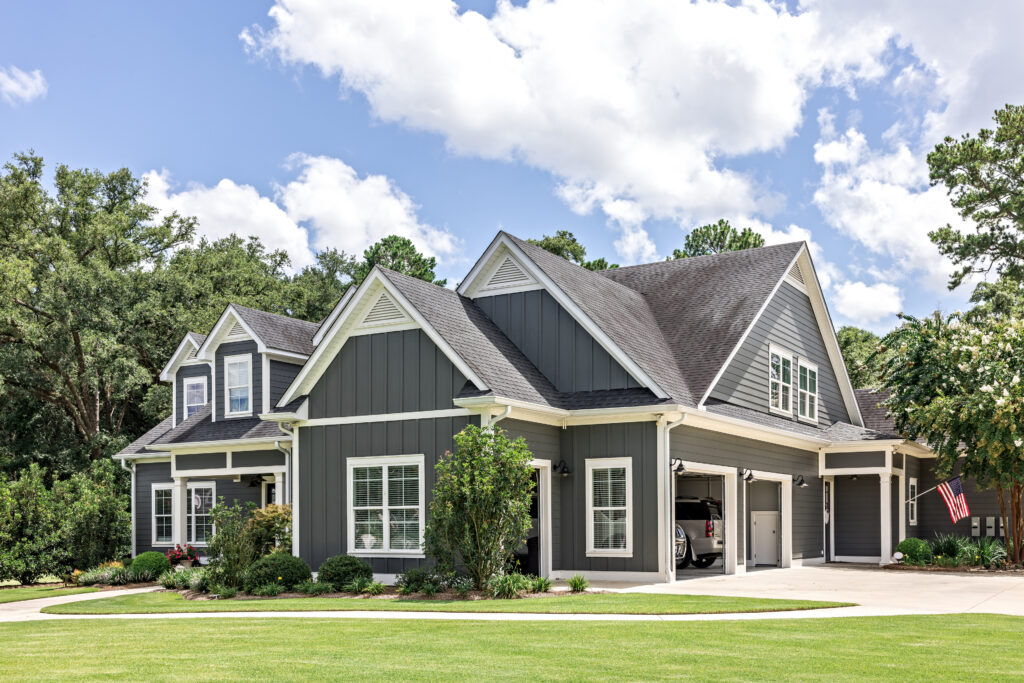A large gray craftsman new construction house with a landscaped yard